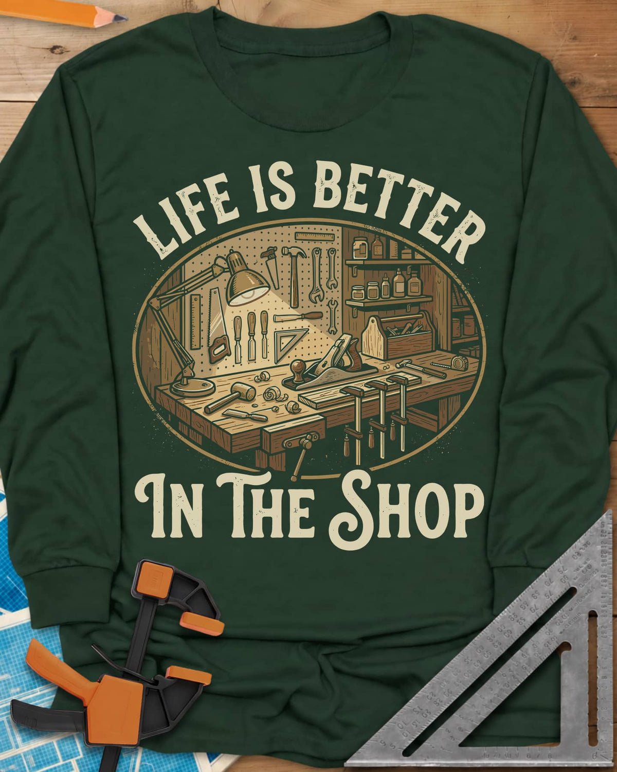 Life Is Better In The Shop long sleeve shirt in Forest Green, a lamp-lit workbench with plane, mallet, clamps and tool