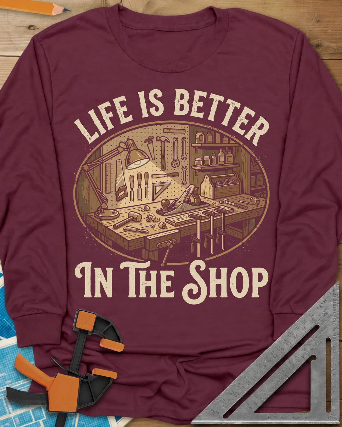 Life Is Better In The Shop long sleeve shirt in Maroon, a lamp-lit workbench with plane, mallet, clamps and tool pegboard