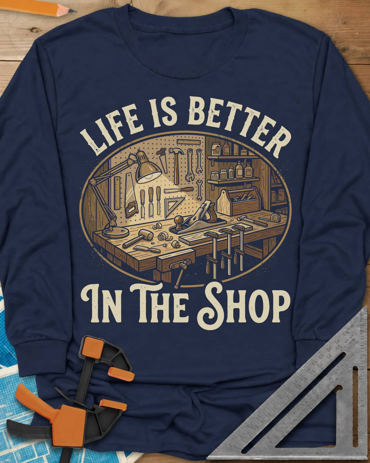 Life Is Better In The Shop long sleeve shirt in Navy, a lamp-lit workbench with plane, mallet, clamps and tool pegboard