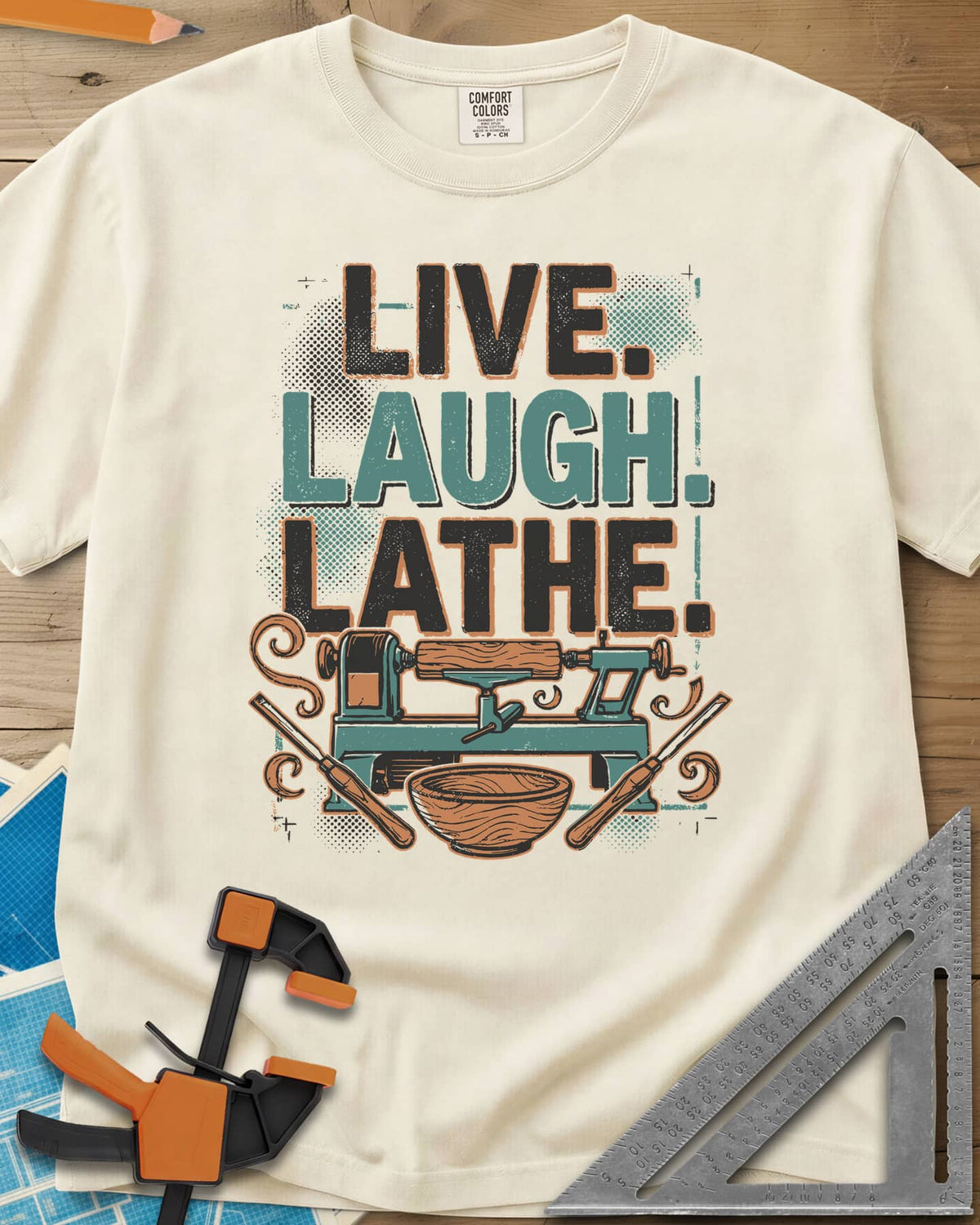 Live. Laugh. Lathe. heavyweight tee in Ivory, a teal wood lathe with a bowl, two gouges and orange wood curls