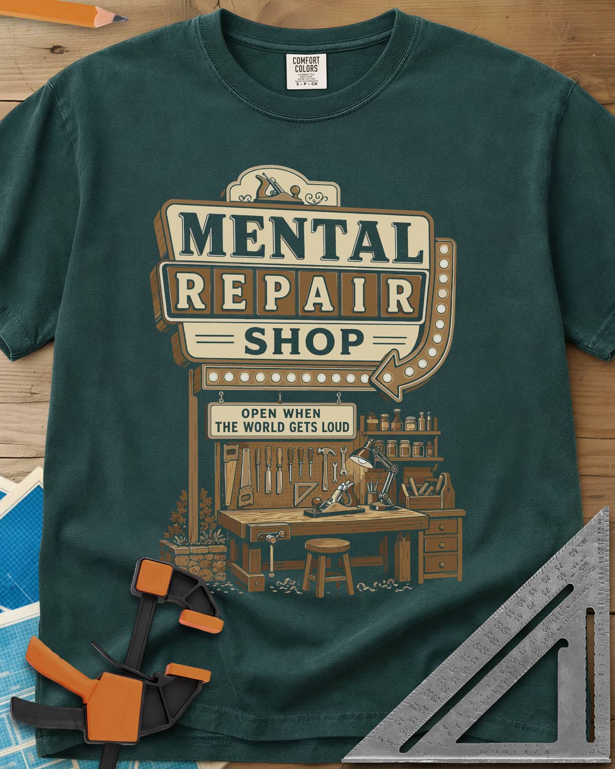 Mental Repair Shop heavyweight tee in Blue Spruce, a retro roadside sign over a tidy woodworking bench and pegboard