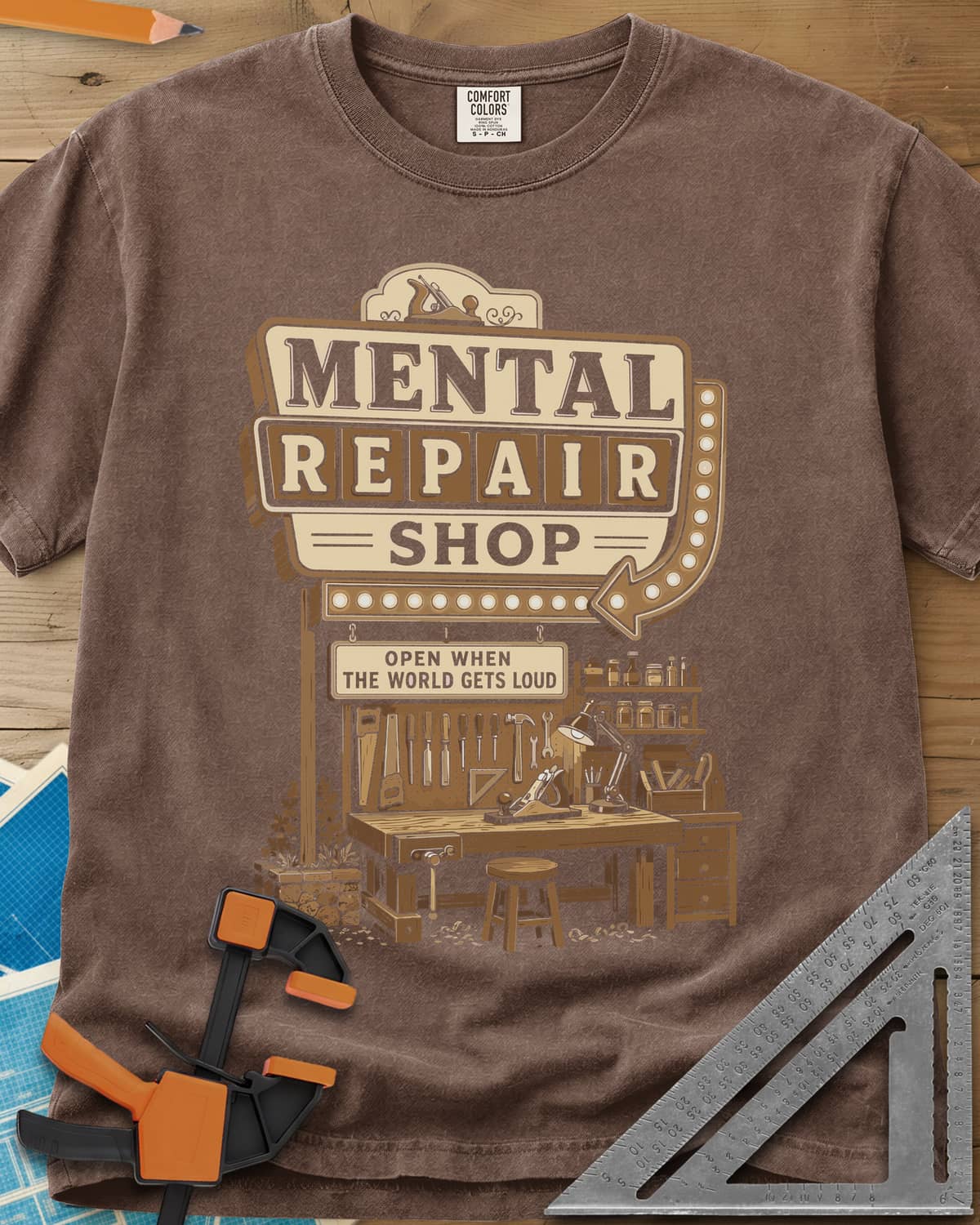 Mental Repair Shop heavyweight tee in Espresso, a retro roadside sign over a tidy woodworking bench and pegboard