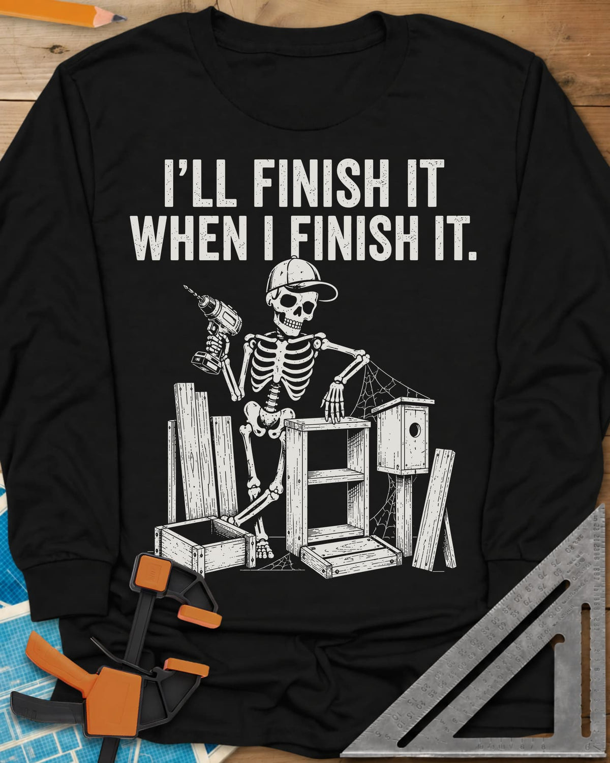 Misses Me At Work long sleeve shirt in Black, a skeleton in a ball cap with a drill among half-built projects
