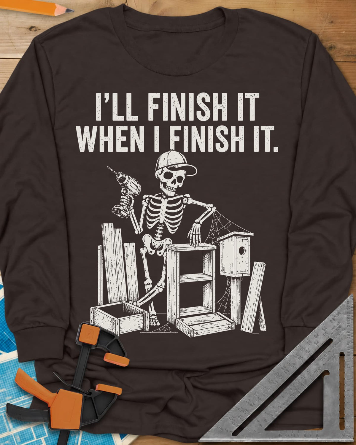 Misses Me At Work long sleeve shirt in Dark Chocolate, a skeleton in a ball cap with a drill among half-built projects
