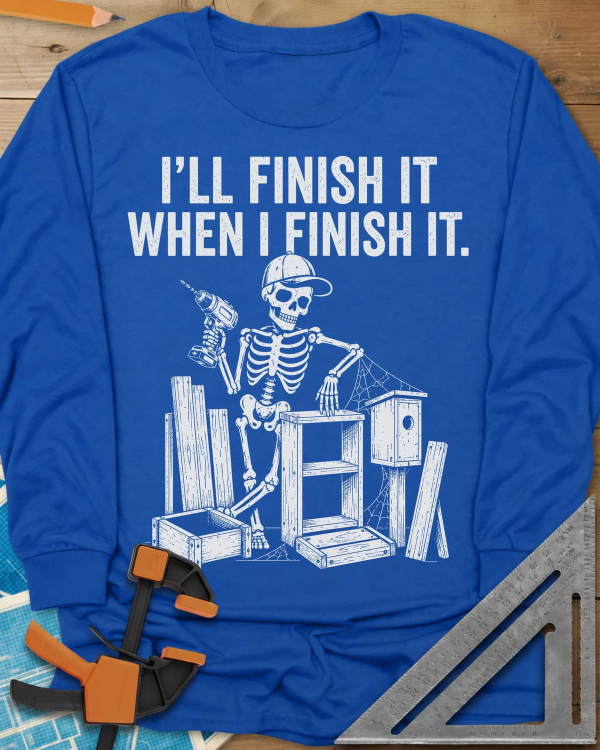 Misses Me At Work long sleeve shirt in Royal, a skeleton in a ball cap with a drill among half-built projects