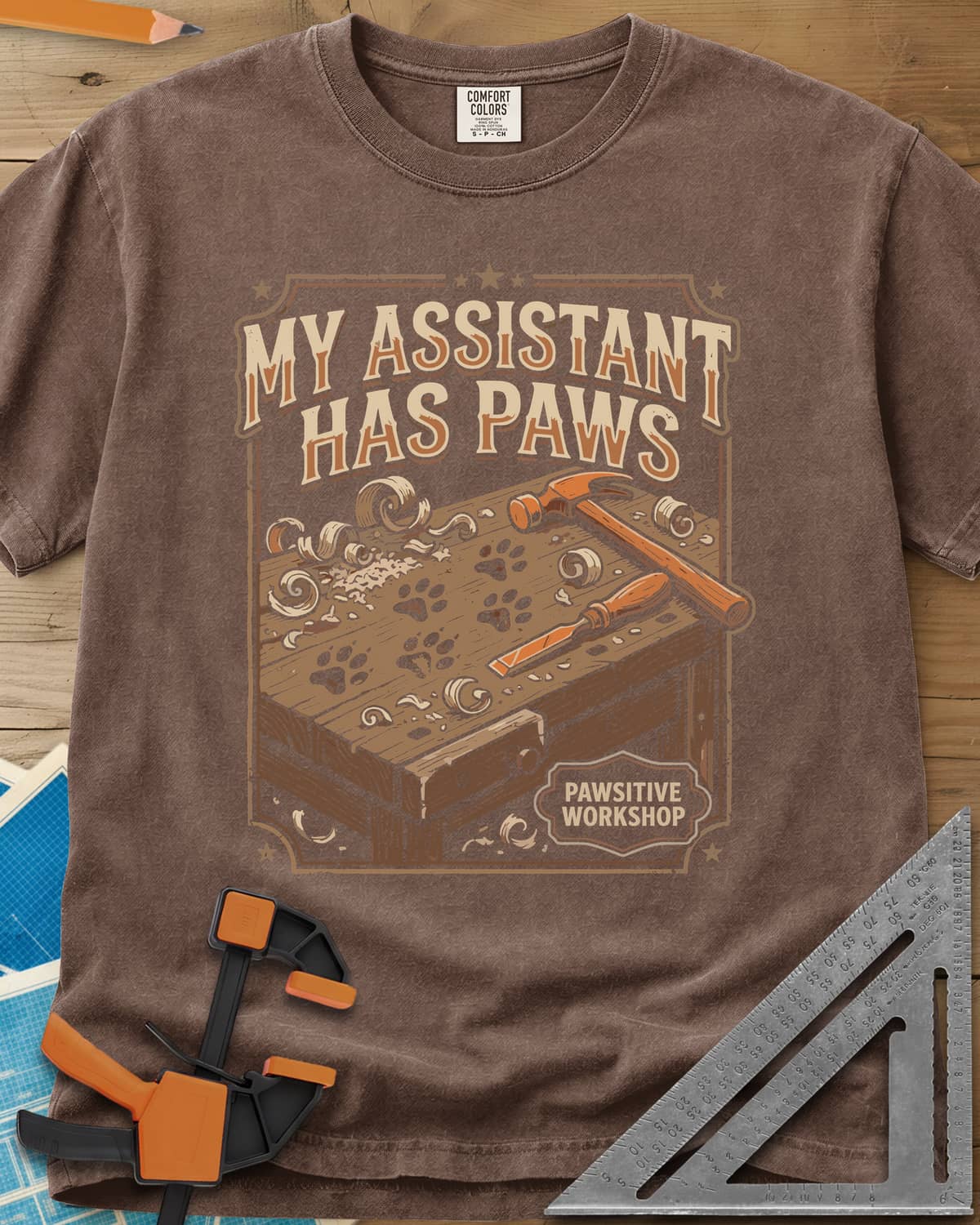 My Assistant Has Paws heavyweight tee in Espresso, workbench with paw prints, shavings, a hammer and a chisel