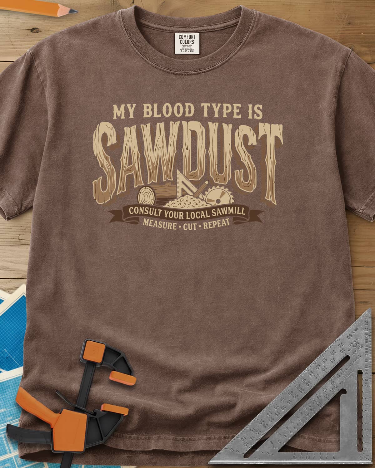 My Blood Type Is Sawdust Woodworking heavyweight tee in Espresso, wood-grain lettering with a log slice, speed square and