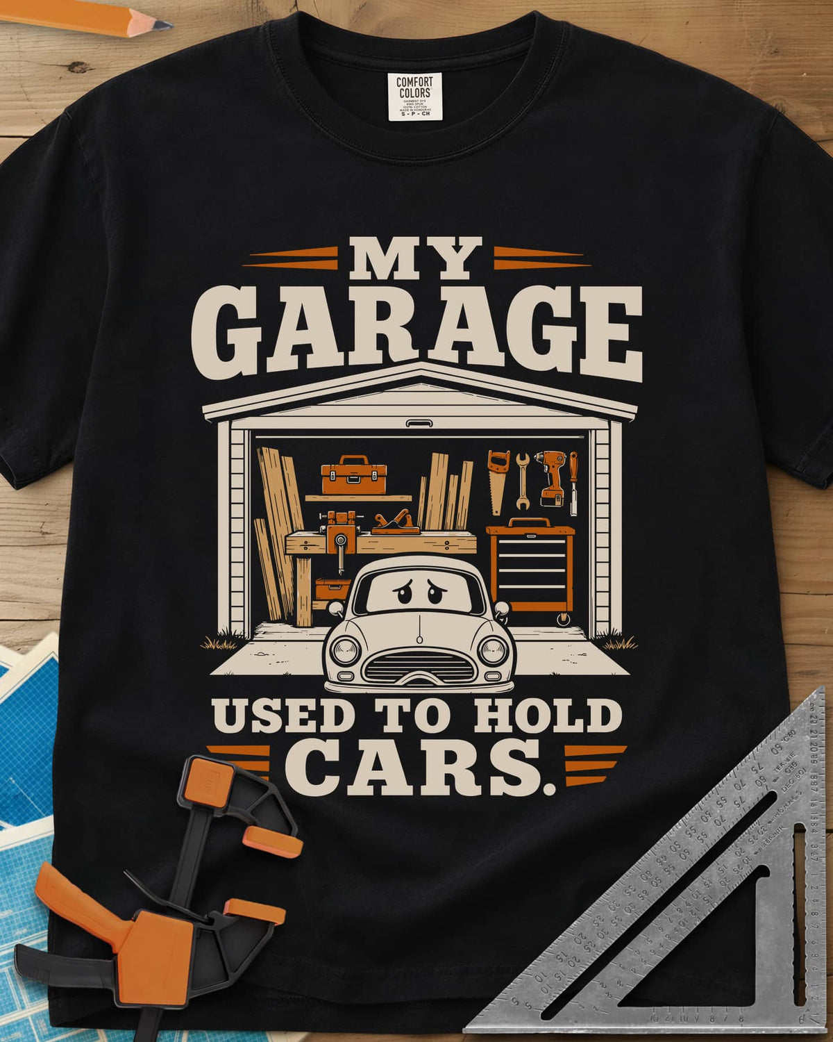 My Garage Used To Hold Cars heavyweight tee in Black, an open garage full of lumber and tools with a worried car