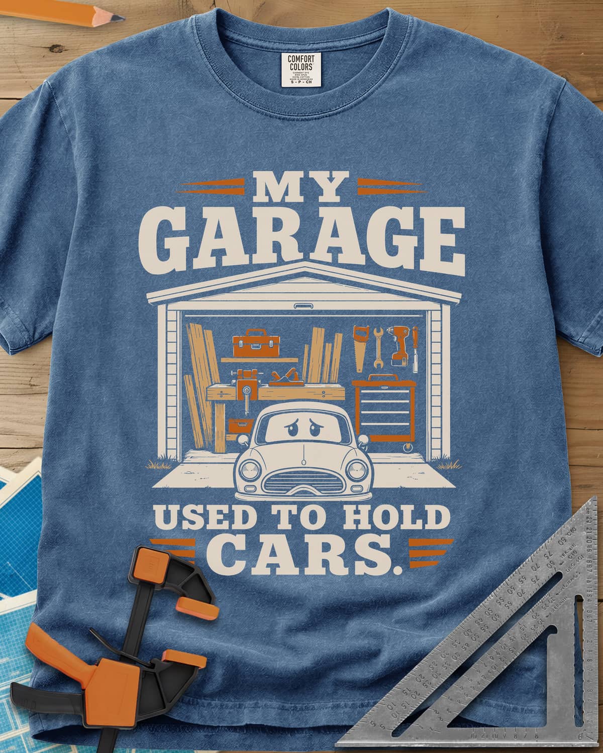 My Garage Used To Hold Cars heavyweight tee in Blue Jean, an open garage full of lumber and tools with a worried car