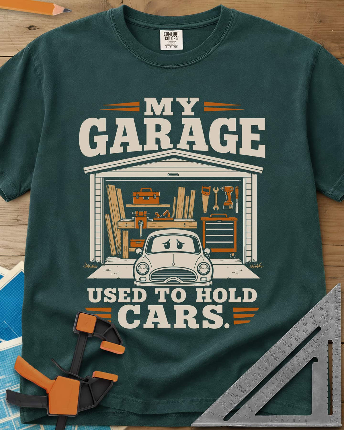 My Garage Used To Hold Cars heavyweight tee in Blue Spruce, an open garage full of lumber and tools with a worried car