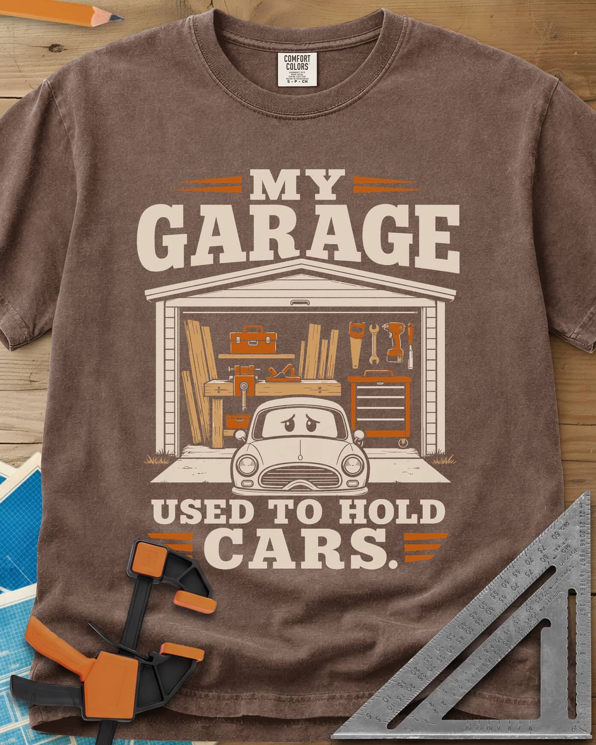My Garage Used To Hold Cars heavyweight tee in Espresso, an open garage full of lumber and tools with a worried car