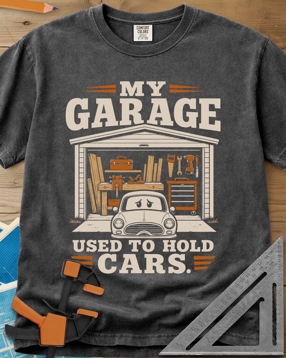 My Garage Used To Hold Cars heavyweight tee in Pepper, an open garage full of lumber and tools with a worried car