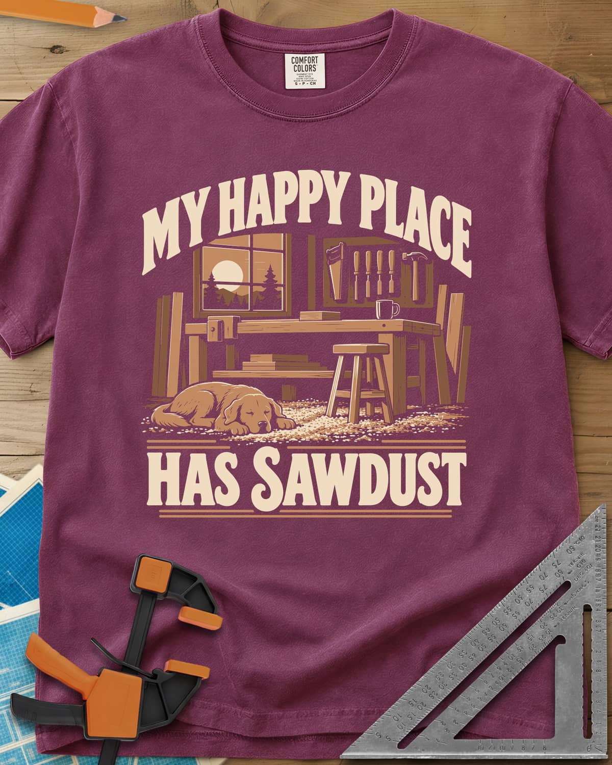 My Happy Place Has Sawdust heavyweight tee in Berry, a shop with a workbench, tool wall and a dog asleep on the sawdust
