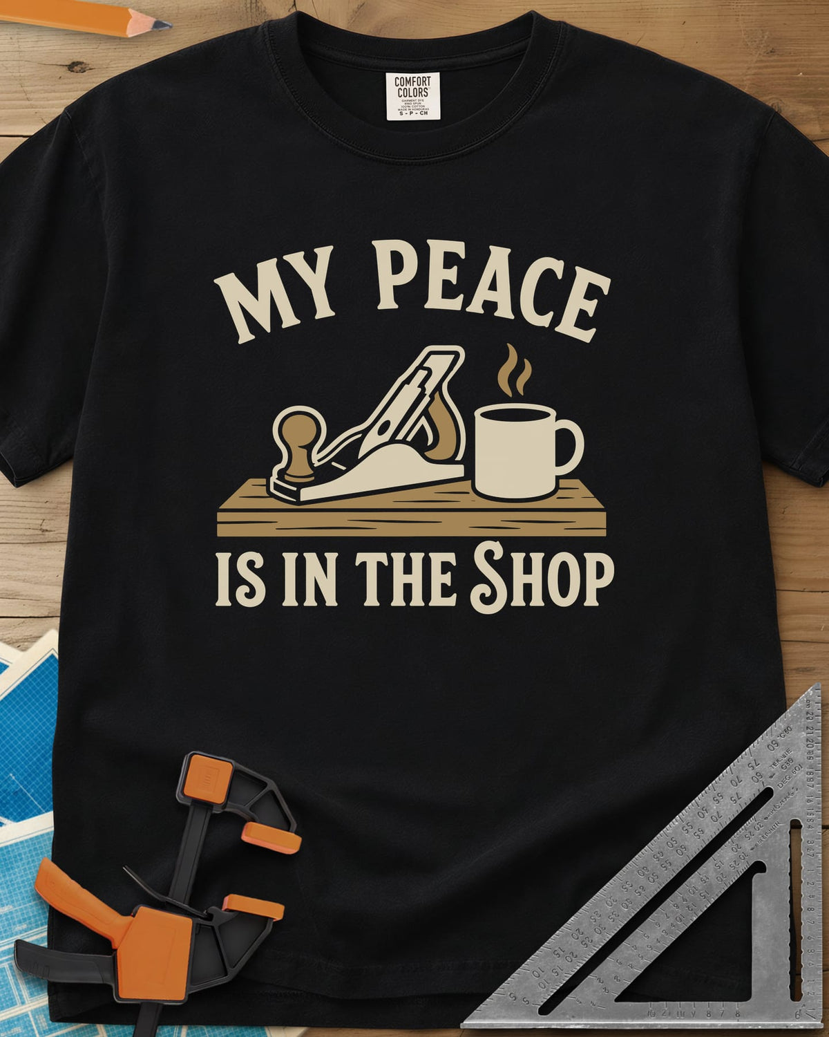 My Peace Is In The Shop heavyweight tee in Black, a hand plane on a plank beside a steaming coffee mug