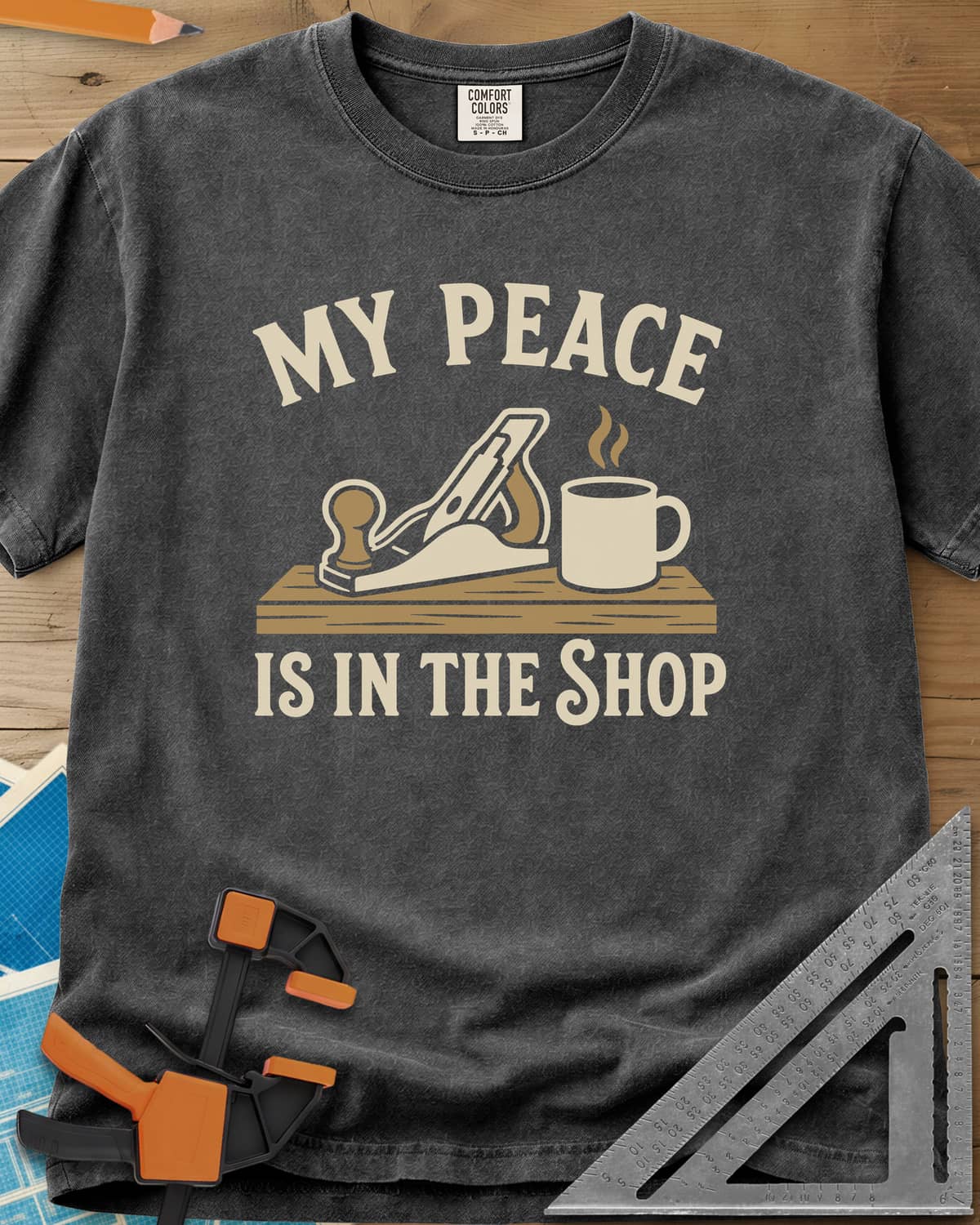 My Peace Is In The Shop heavyweight tee in Pepper, a hand plane on a plank beside a steaming coffee mug