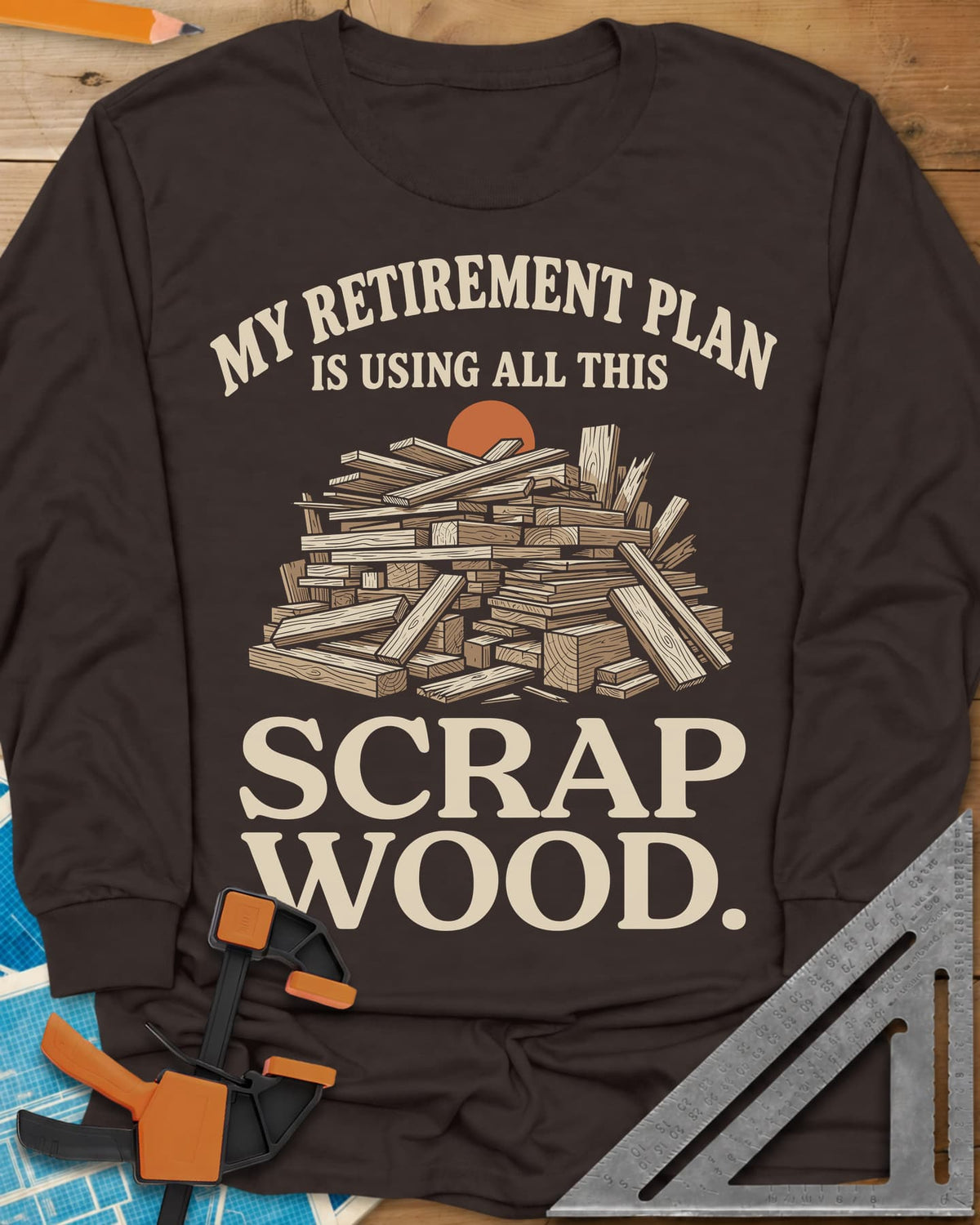 My Retirement Plan Scrap Wood long sleeve shirt in Dark Chocolate, a heaped pile of scrap boards in front of a setting sun