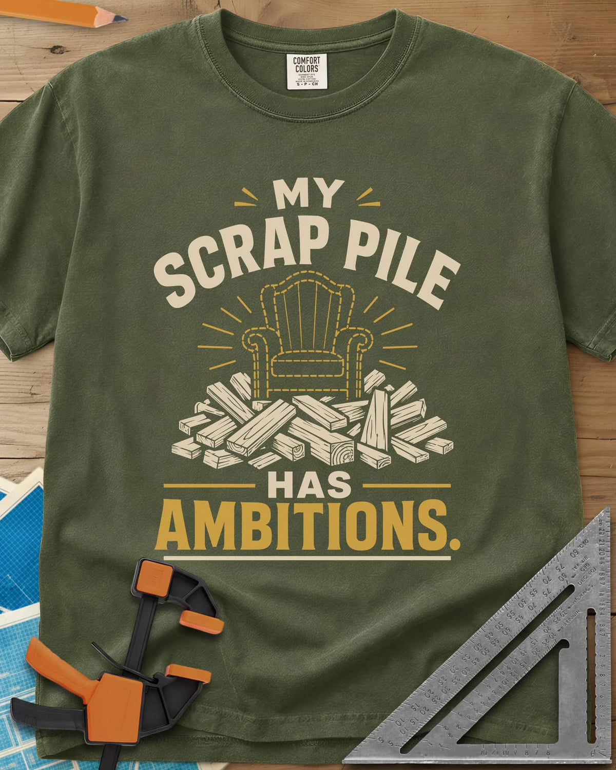 My Scrap Pile Has Ambitions heavyweight tee in Hemp, a dotted gold armchair outline rising from a pile of wood offcuts