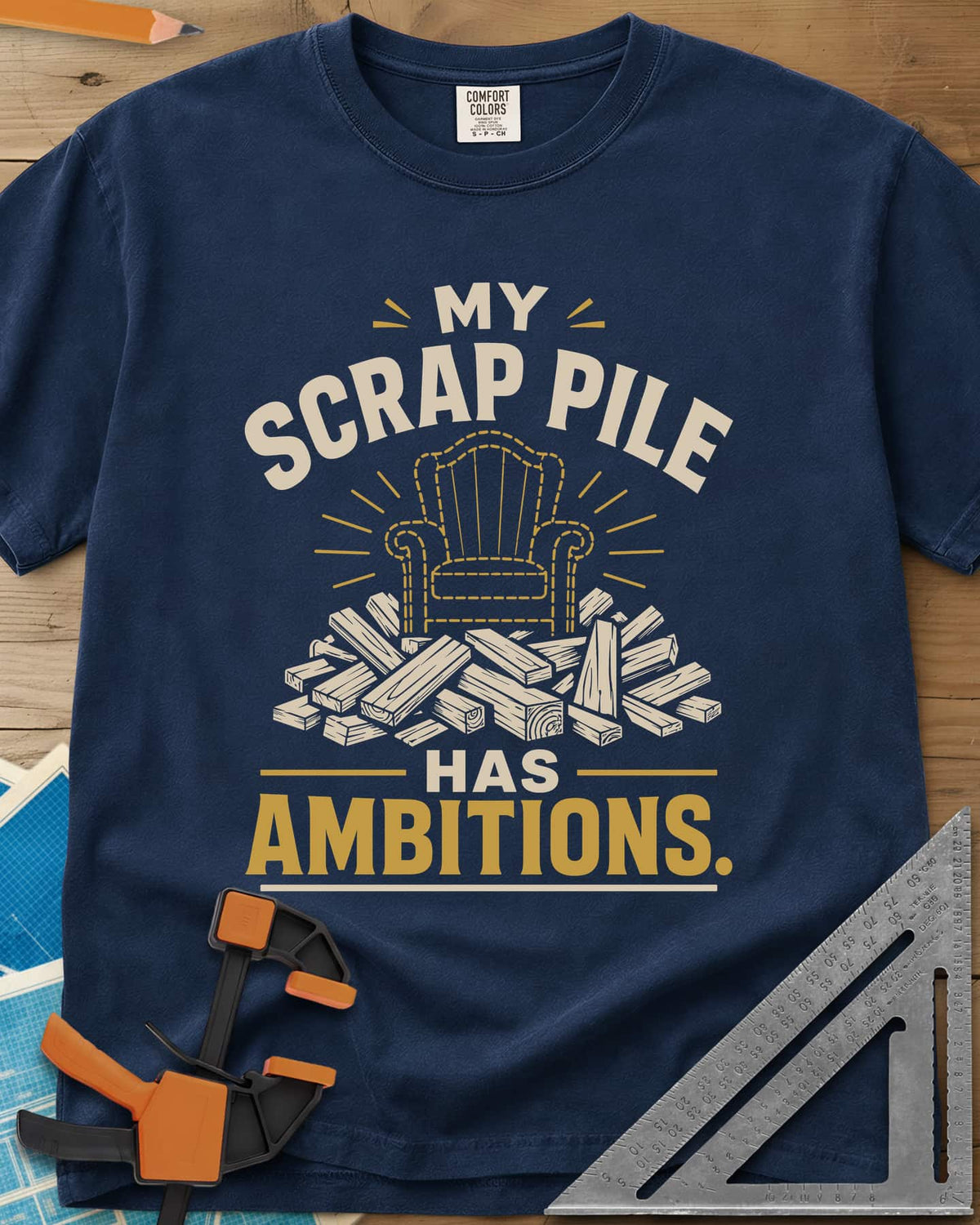 My Scrap Pile Has Ambitions heavyweight tee in Navy, a dotted gold armchair outline rising from a pile of wood offcuts
