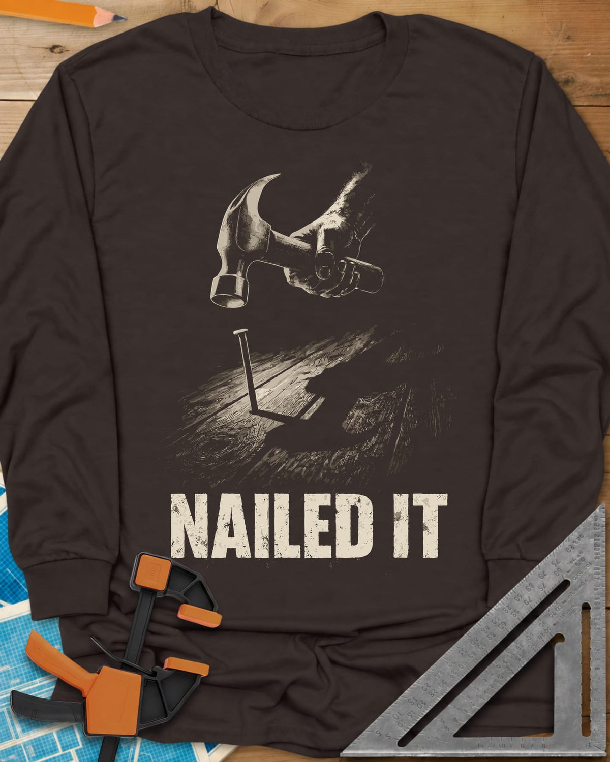 Nailed It Hammer long sleeve shirt in Dark Chocolate, a hand raising a claw hammer over a nail in rough boards
