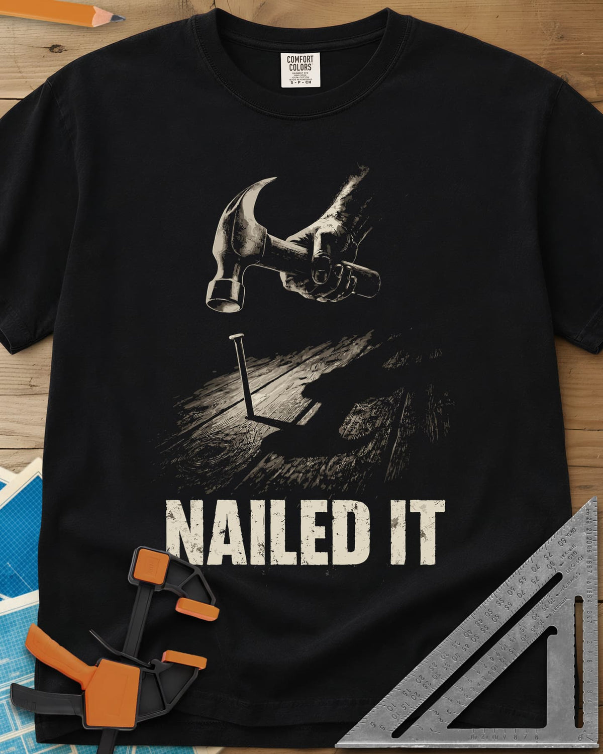 Nailed It Hammer heavyweight tee in Black, a hand raising a claw hammer over a nail in rough boards