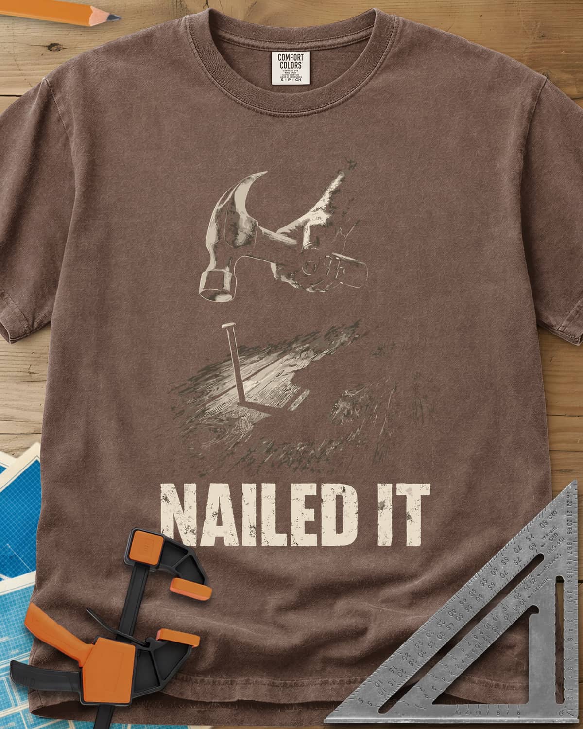 Nailed It Hammer heavyweight tee in Espresso, a hand raising a claw hammer over a nail in rough boards
