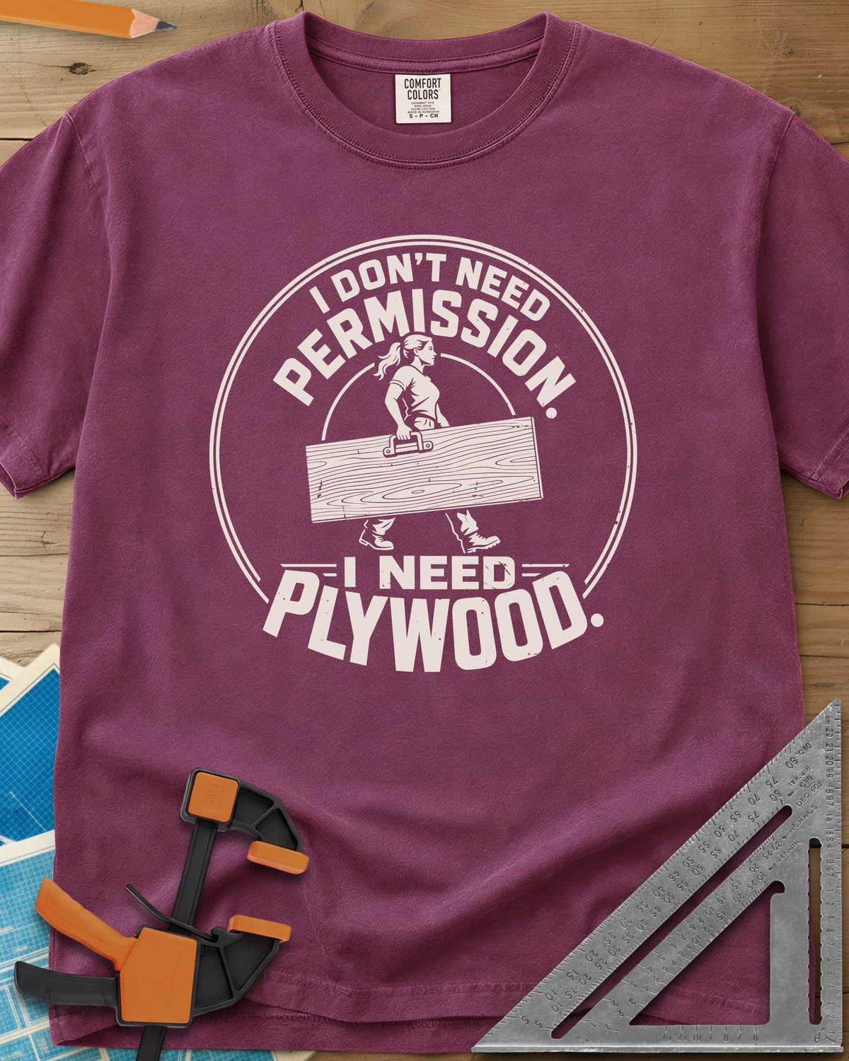 Need Plywood heavyweight tee in Berry, a woman with a ponytail carrying a plywood sheet in a round badge