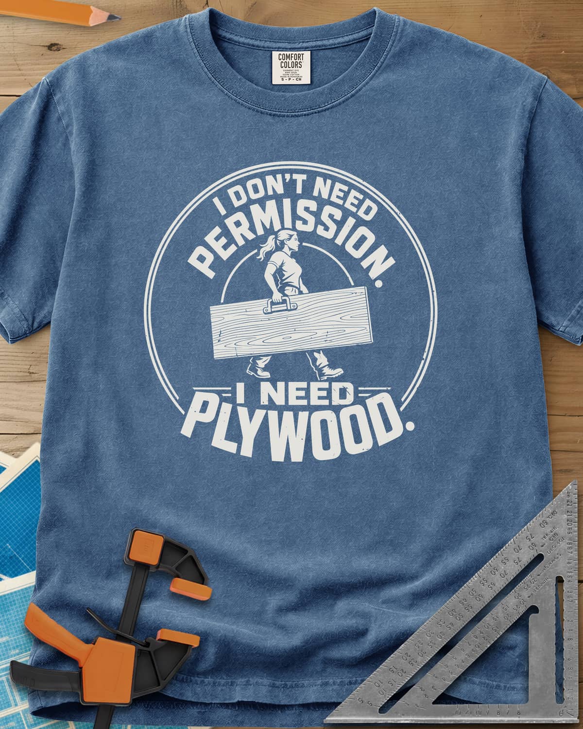 Need Plywood heavyweight tee in Blue Jean, a woman with a ponytail carrying a plywood sheet in a round badge