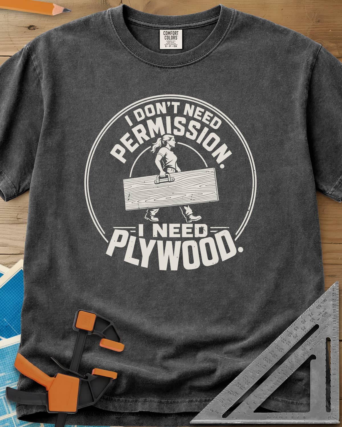 Need Plywood heavyweight tee in Pepper, a woman with a ponytail carrying a plywood sheet in a round badge