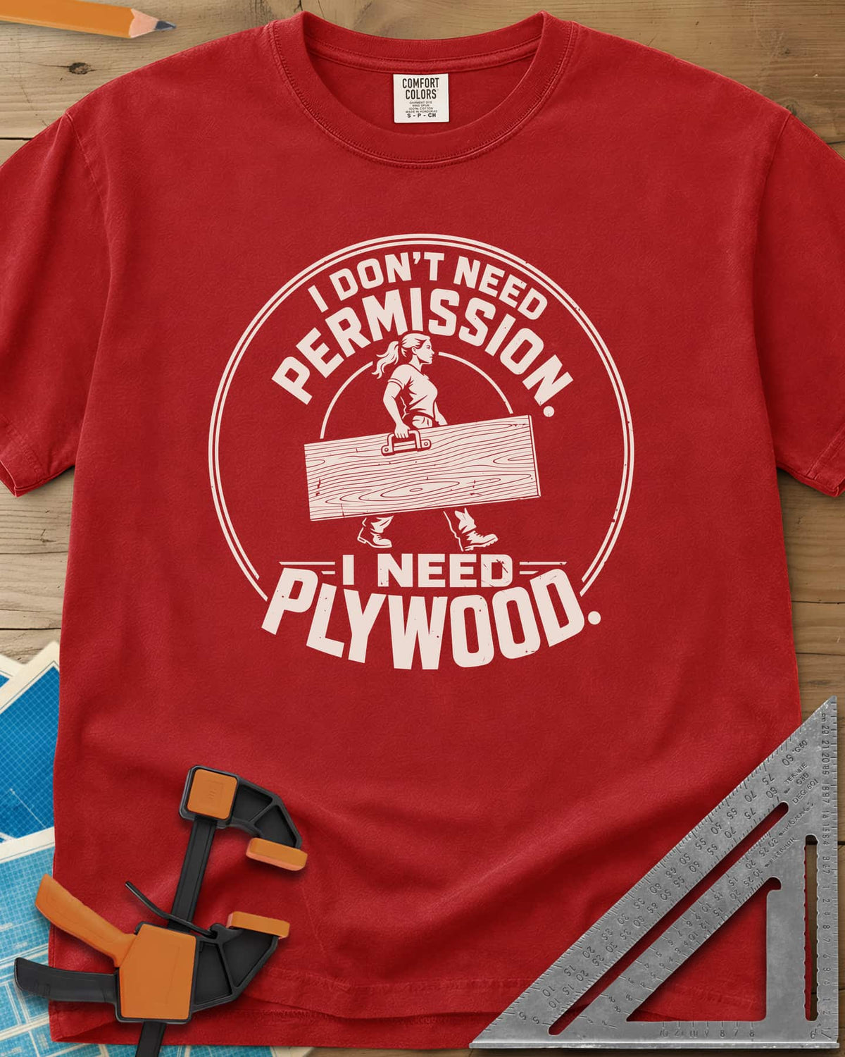 Need Plywood heavyweight tee in Red, a woman with a ponytail carrying a plywood sheet in a round badge