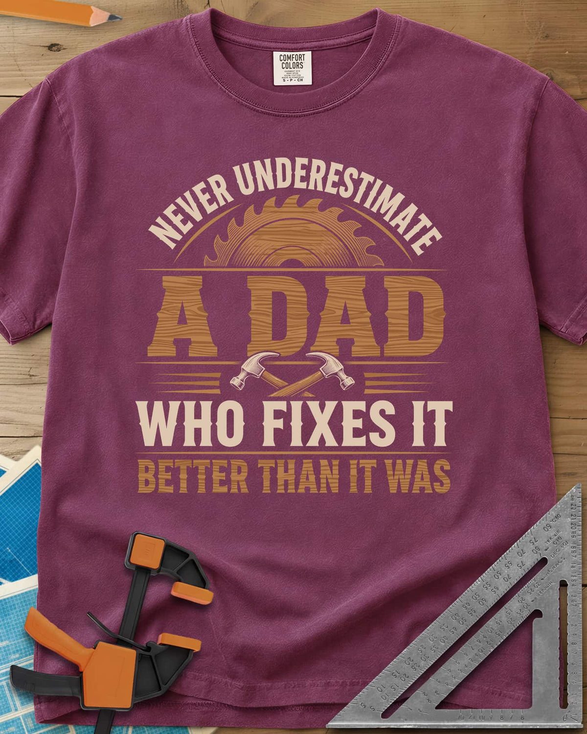 Never Underestimate A Dad Who Fixes It heavyweight tee in Berry, saw blade and two crossed hammers around wood-grain