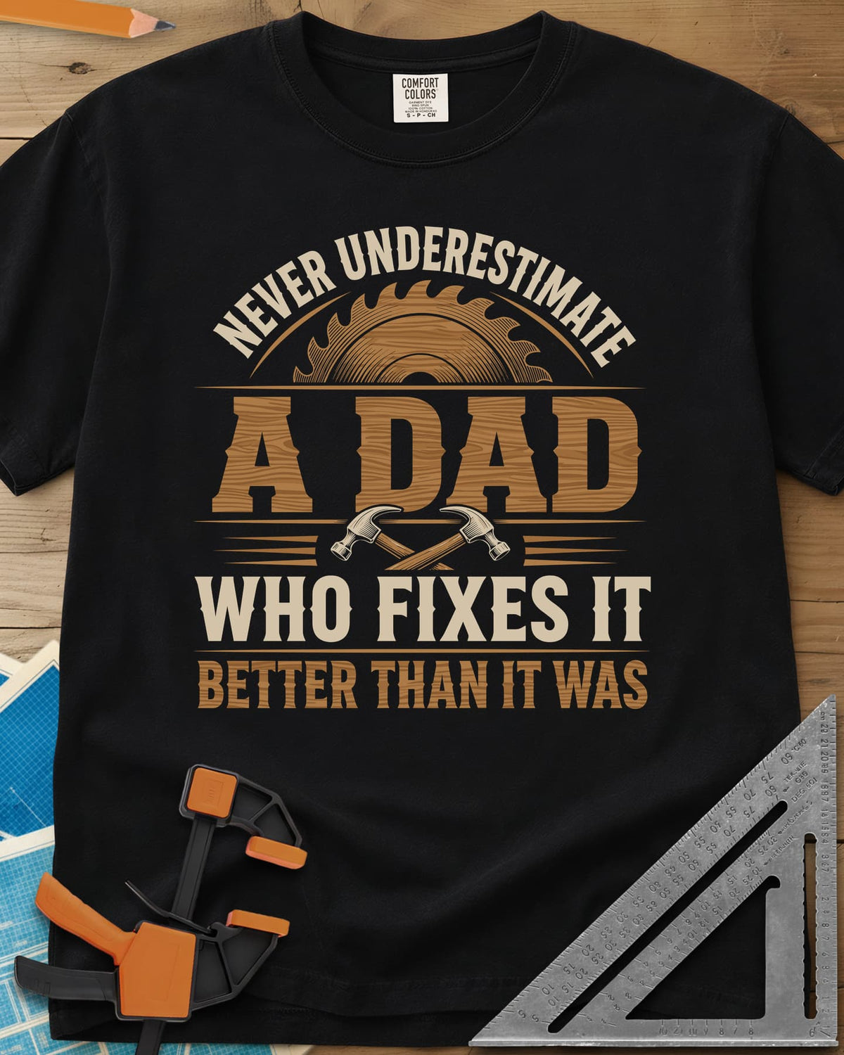 Never Underestimate A Dad Who Fixes It heavyweight tee in Black, saw blade and two crossed hammers around wood-grain