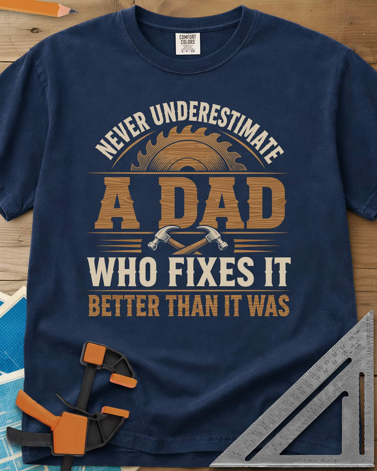 Never Underestimate A Dad Who Fixes It heavyweight tee in Navy, saw blade and two crossed hammers around wood-grain lettering