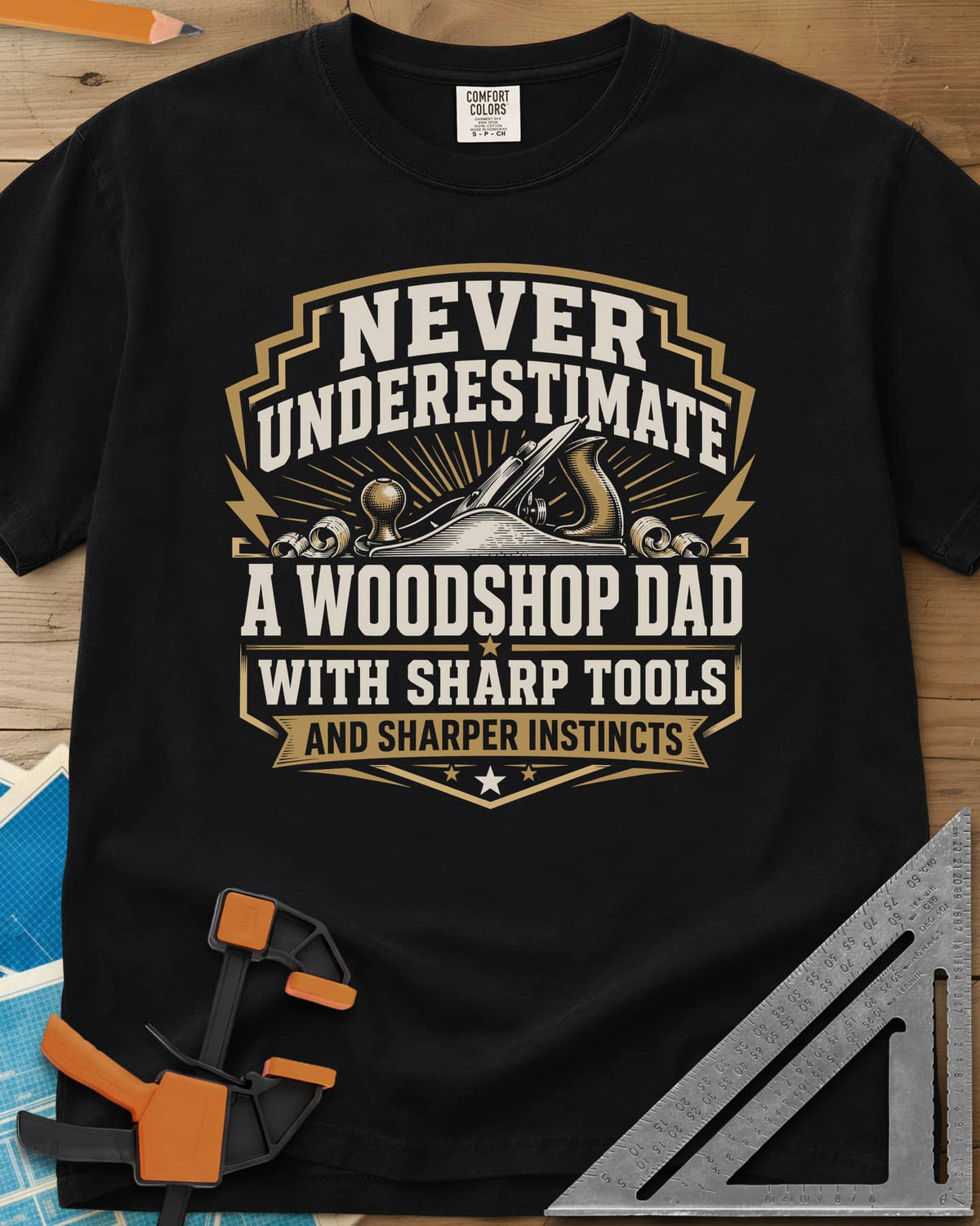 Never Underestimate A Woodshop Dad heavyweight tee in Black, a shield badge with a hand plane, wood curls and sunburst rays