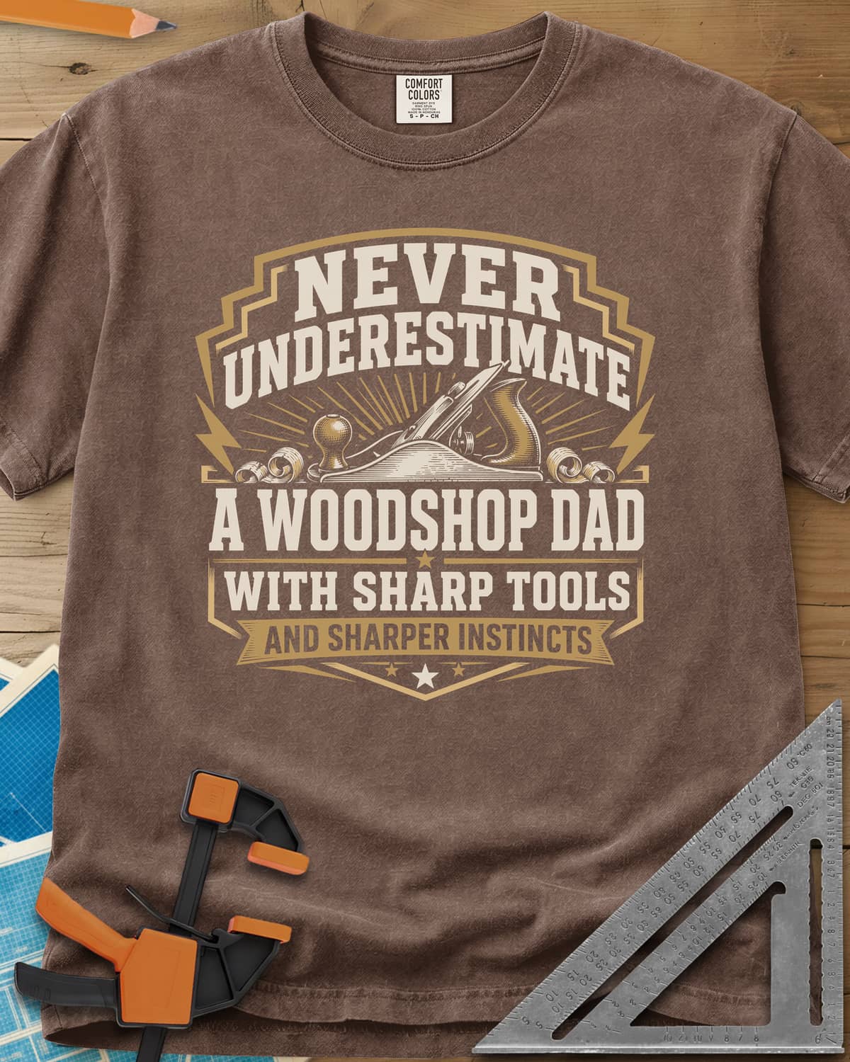 Never Underestimate A Woodshop Dad heavyweight tee in Espresso, a shield badge with a hand plane, wood curls and sunburst