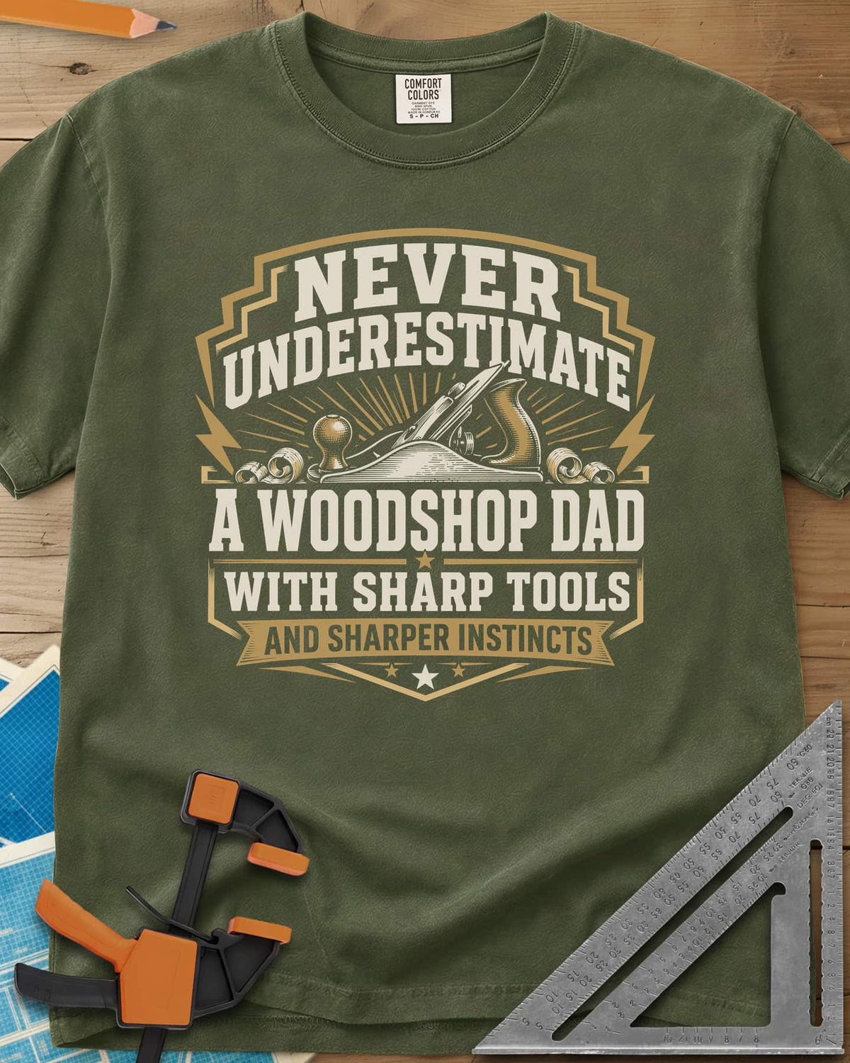 Never Underestimate A Woodshop Dad heavyweight tee in Hemp, a shield badge with a hand plane, wood curls and sunburst rays