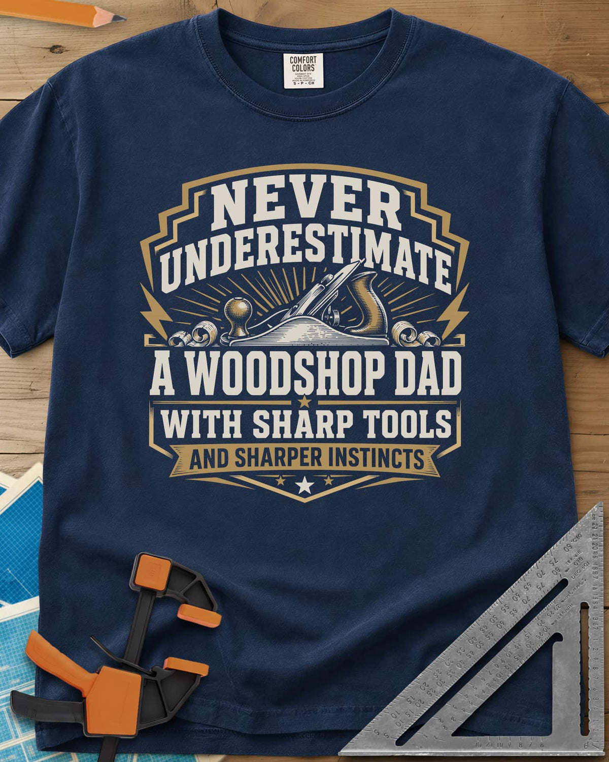 Never Underestimate A Woodshop Dad heavyweight tee in Navy, a shield badge with a hand plane, wood curls and sunburst rays