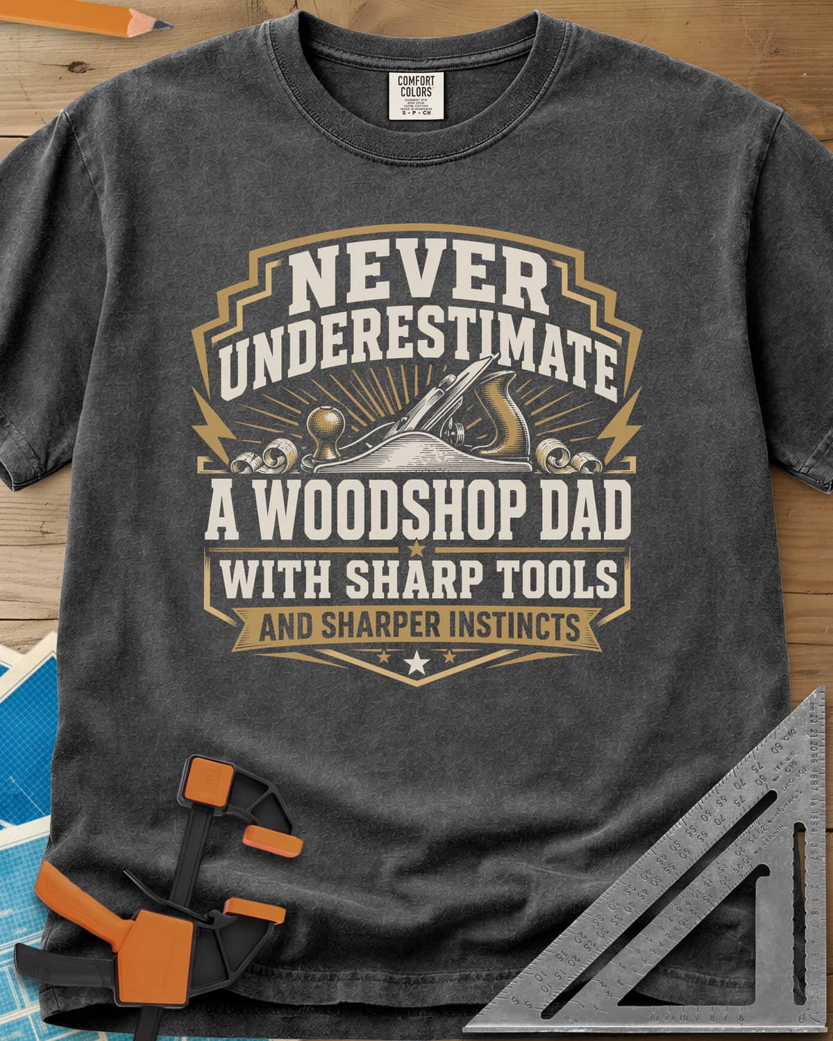 Never Underestimate A Woodshop Dad heavyweight tee in Pepper, a shield badge with a hand plane, wood curls and sunburst rays