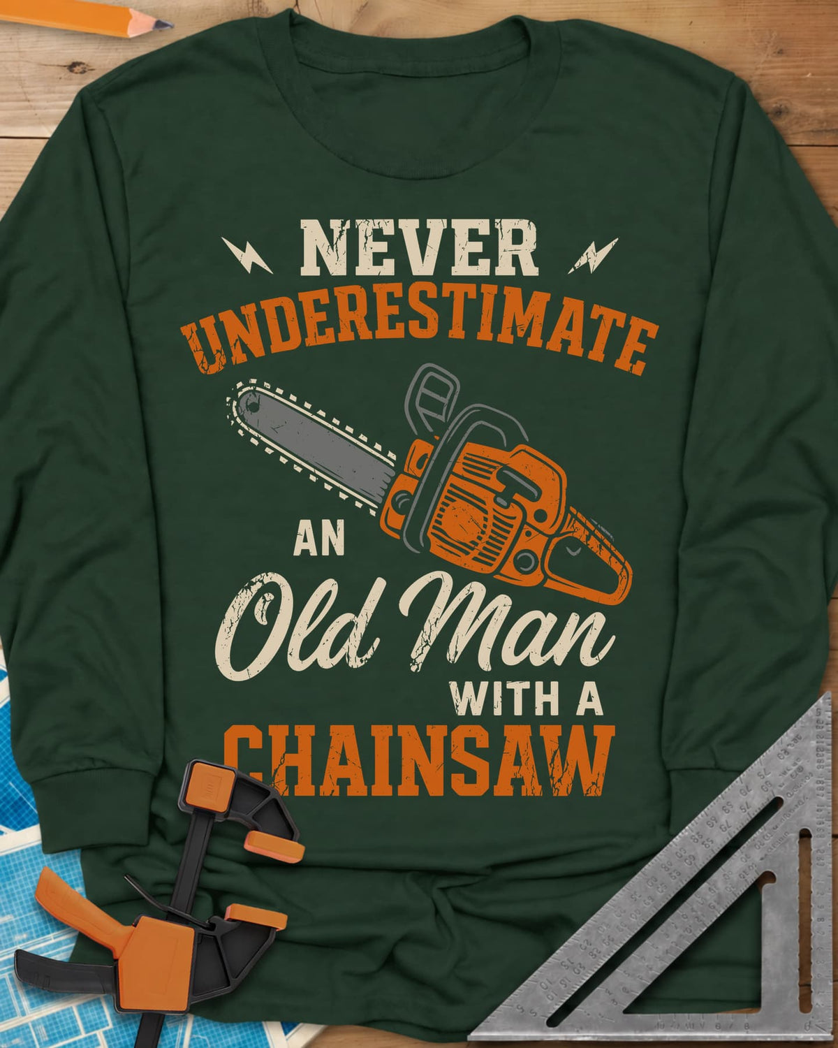 Never Underestimate an Old Man With a Chainsaw long sleeve shirt in Forest Green, an orange chainsaw between lightning bolts
