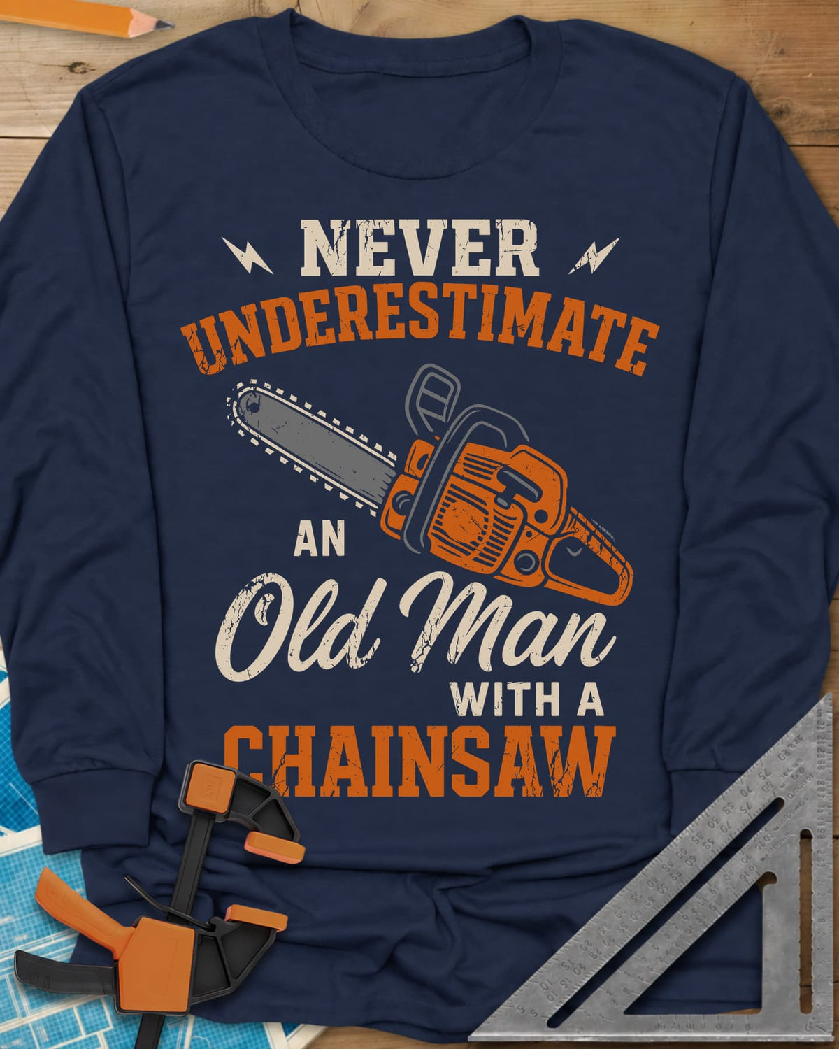 Never Underestimate an Old Man With a Chainsaw long sleeve shirt in Navy, an orange chainsaw between lightning bolts and