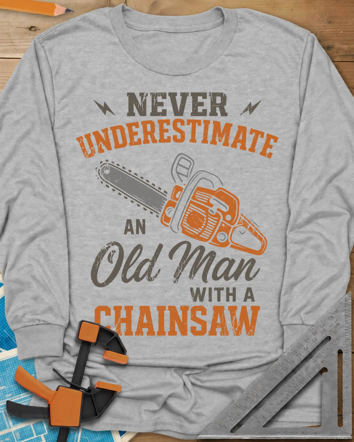 Never Underestimate an Old Man With a Chainsaw long sleeve shirt in Sport Grey, an orange chainsaw between lightning bolts