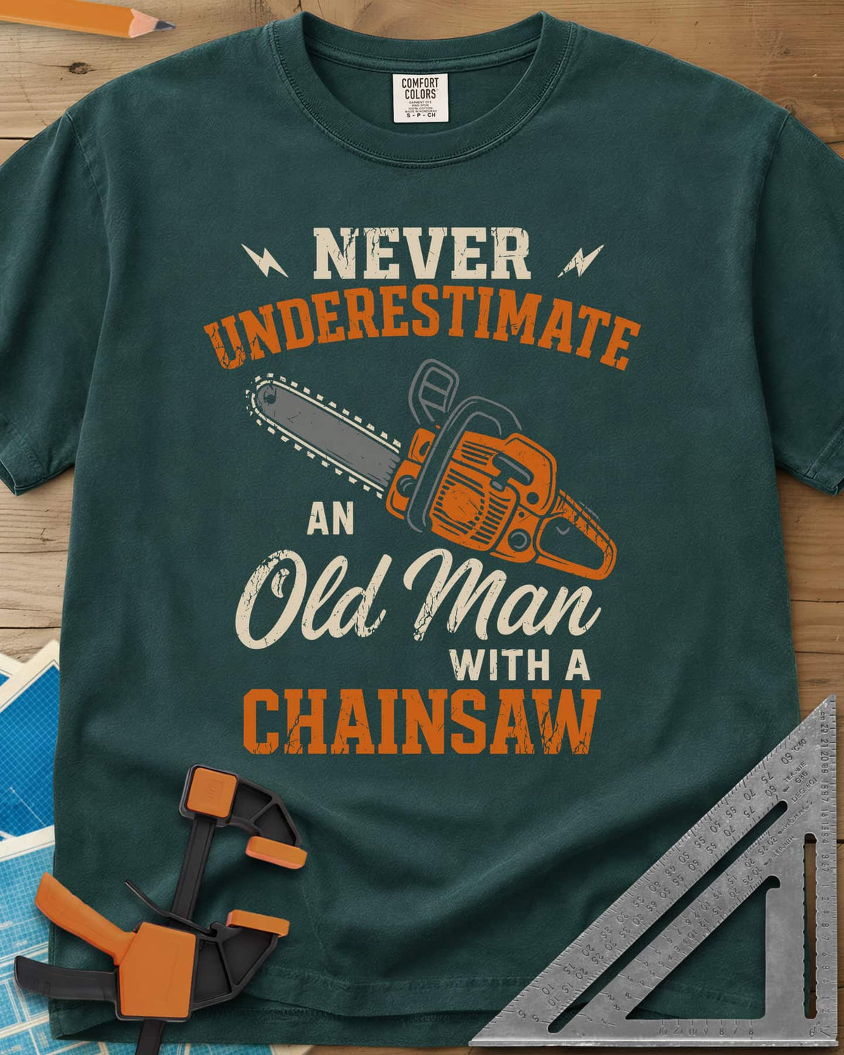 Never Underestimate an Old Man With a Chainsaw heavyweight tee in Blue Spruce, an orange chainsaw between lightning bolts