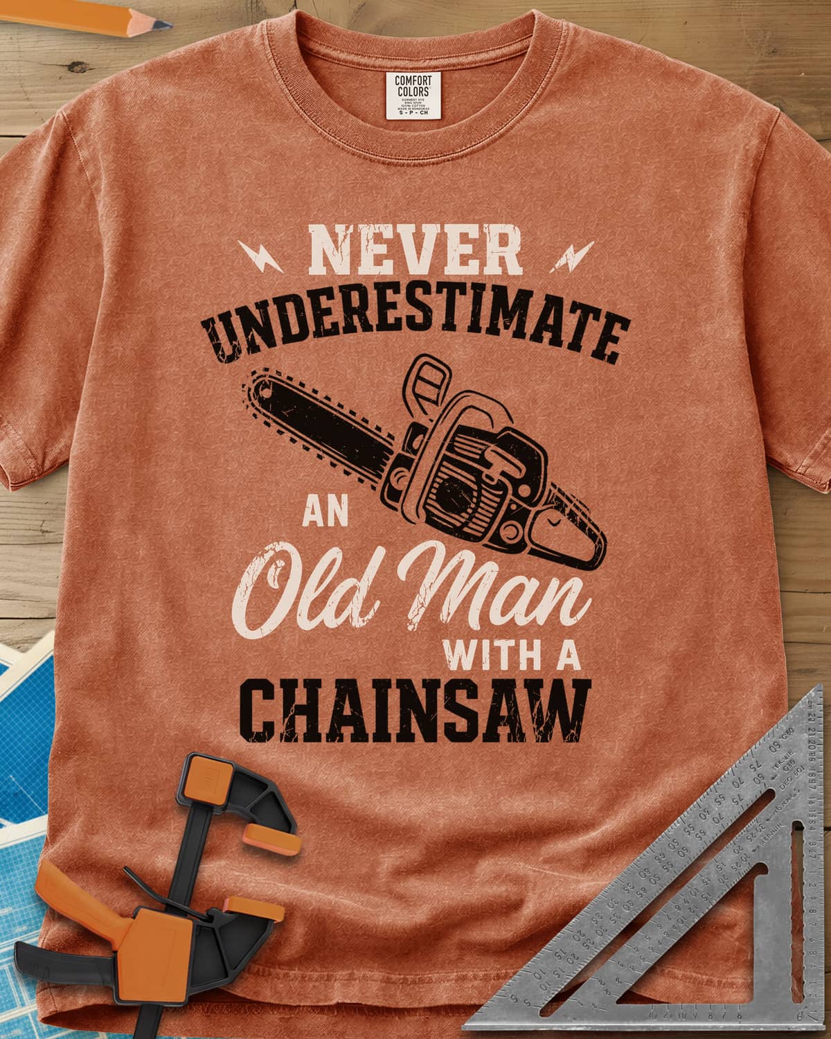 Never Underestimate an Old Man With a Chainsaw heavyweight tee in Yam, an orange chainsaw between lightning bolts and mixed