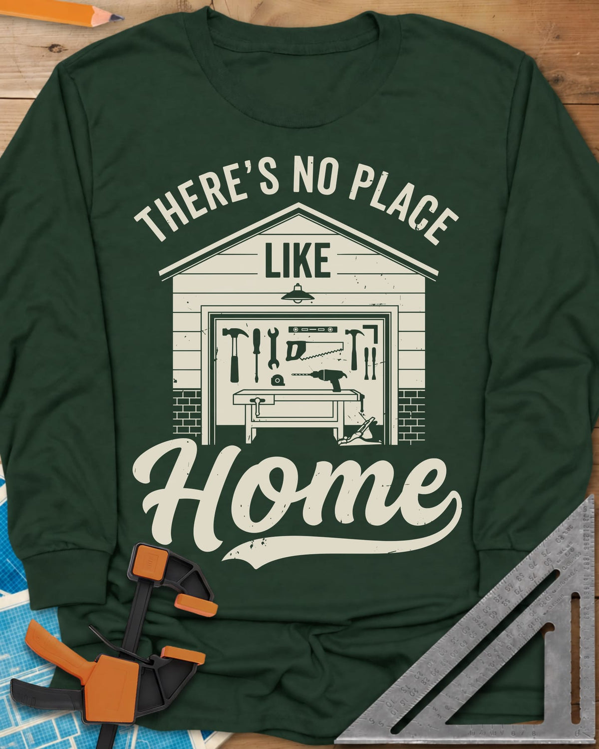 No Place Like Home long sleeve shirt in Forest Green, a garage with its door up on a tool wall, above script Home