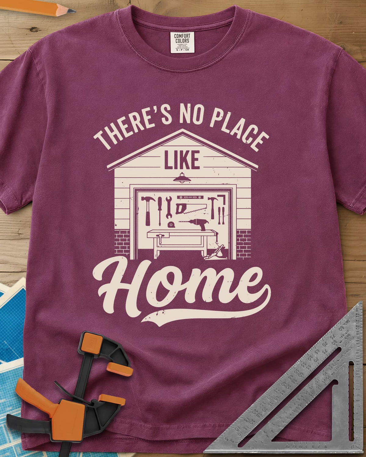 No Place Like Home heavyweight tee in Berry, a garage with its door up on a tool wall, above script Home