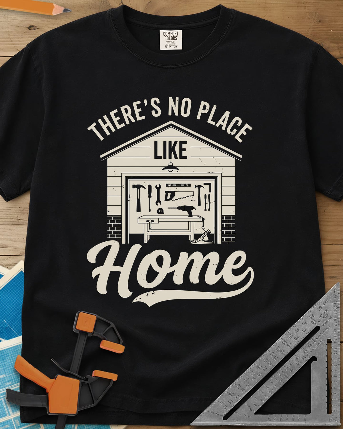 No Place Like Home heavyweight tee in Black, a garage with its door up on a tool wall, above script Home