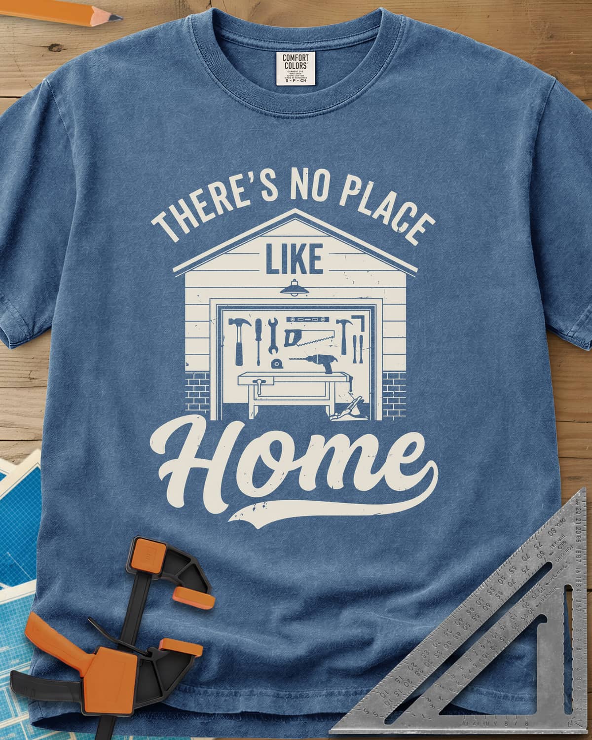 No Place Like Home heavyweight tee in Blue Jean, a garage with its door up on a tool wall, above script Home