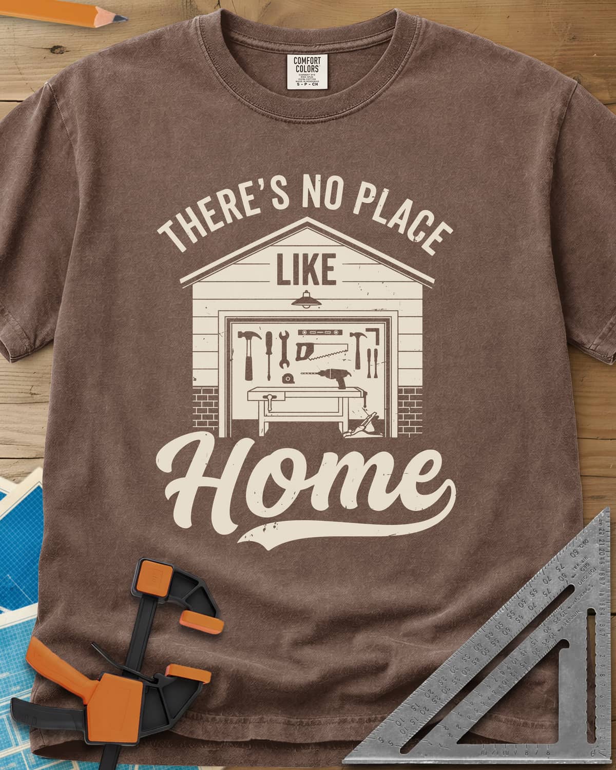 No Place Like Home heavyweight tee in Espresso, a garage with its door up on a tool wall, above script Home