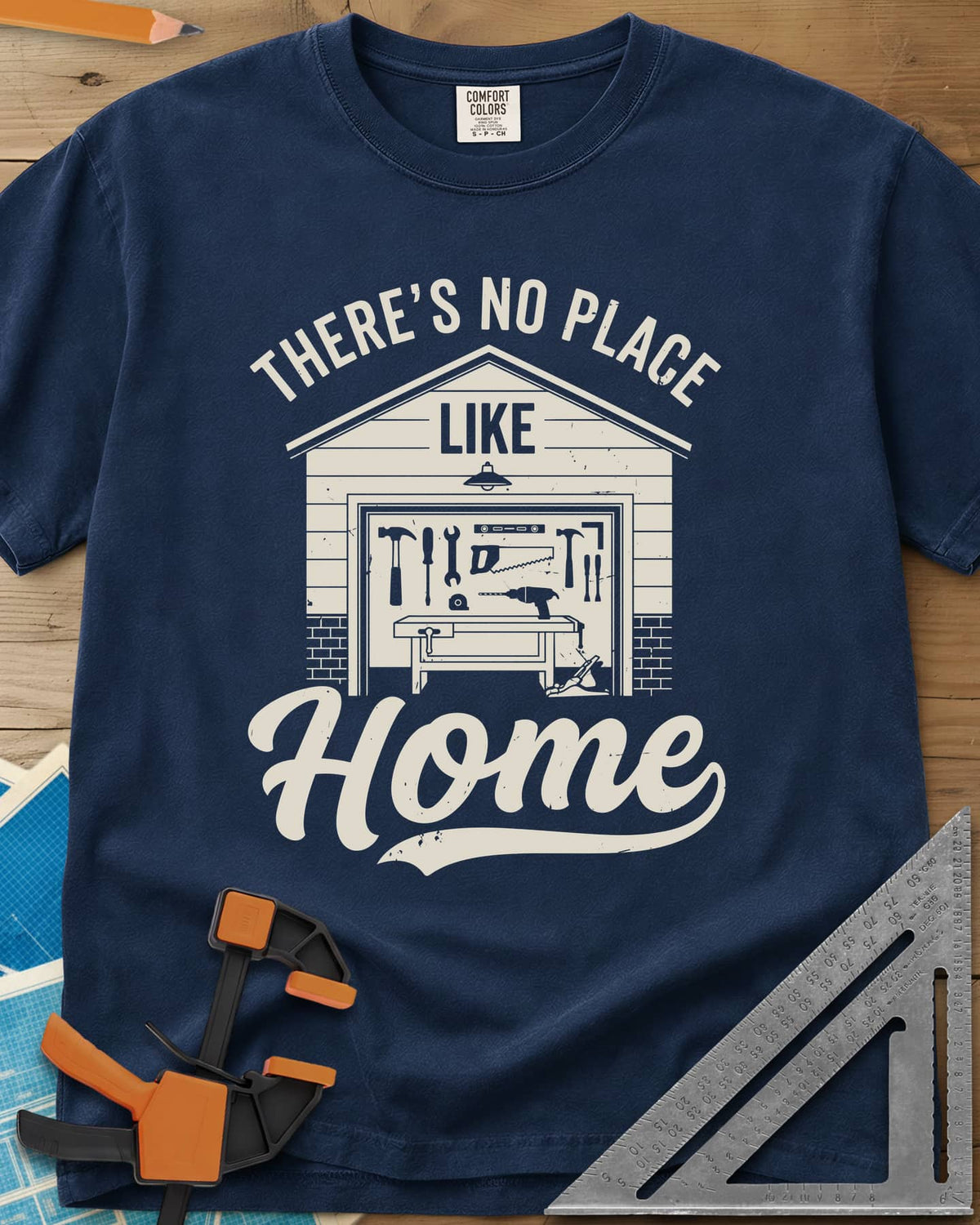 No Place Like Home heavyweight tee in Navy, a garage with its door up on a tool wall, above script Home