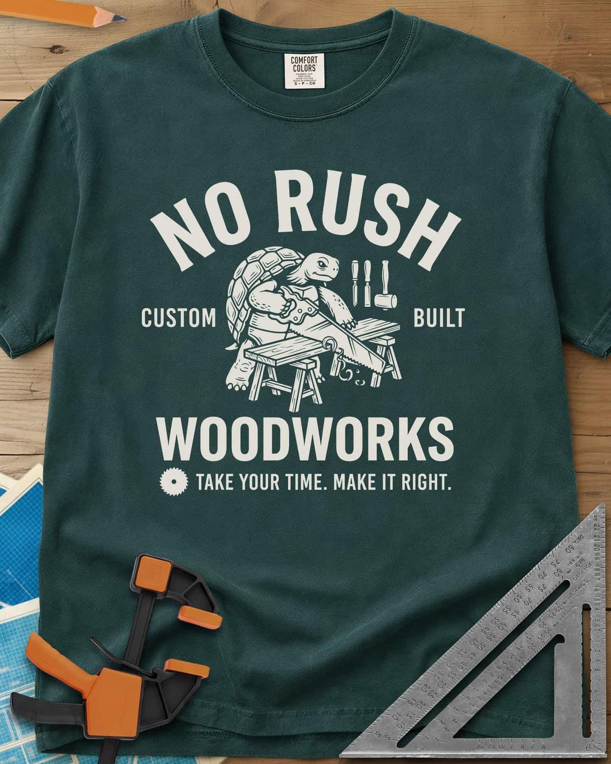 No Rush Woodworks heavyweight tee in Blue Spruce, a tortoise sawing a board on sawhorses inside a woodshop badge