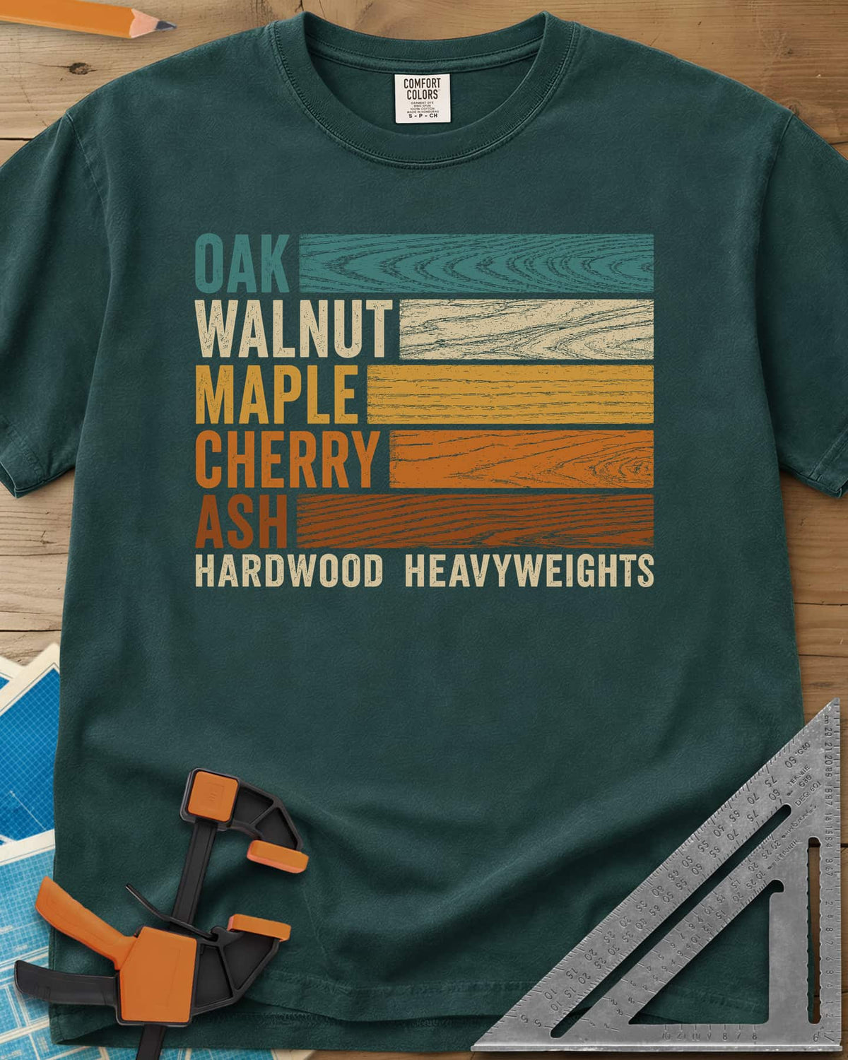 Oak Walnut Maple Cherry Ash heavyweight tee in Blue Spruce, five wood names beside strips of their own grain in retro colors